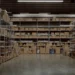 rows of shelves stocked with uniform boxes in a vast, organized warehouse, illuminated by overhead lights.